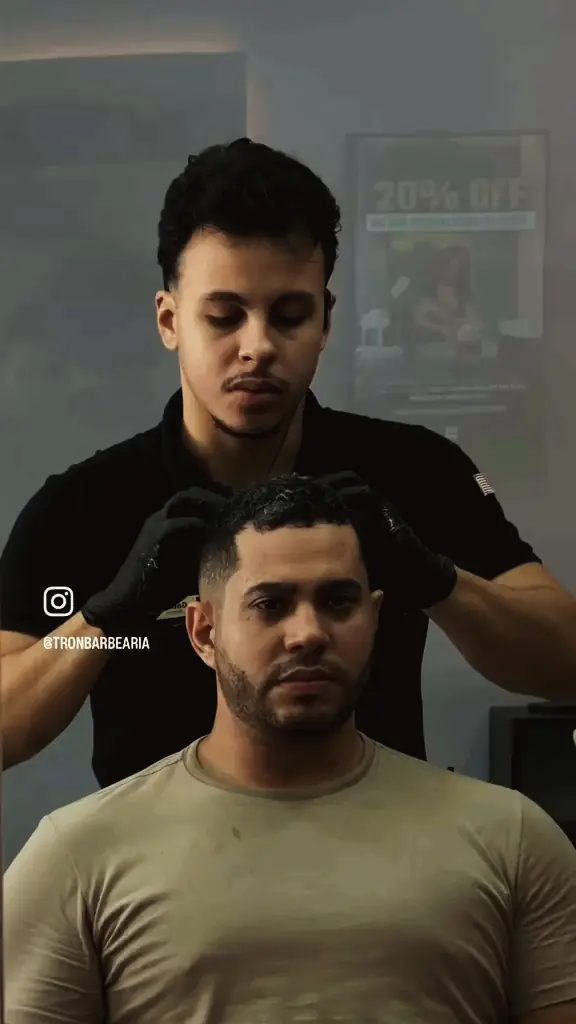 Barbeiro de luvas pretas preparando o cabelo de um cliente sentado na cadeira