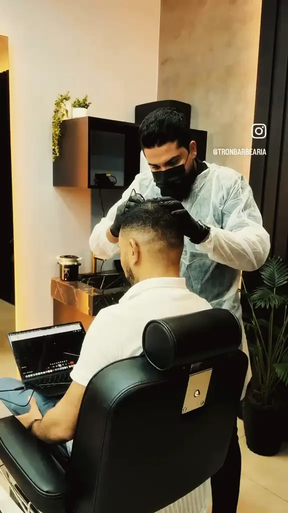 Profissional de máscara e avental aplicando tratamento capilar em cliente na cadeira