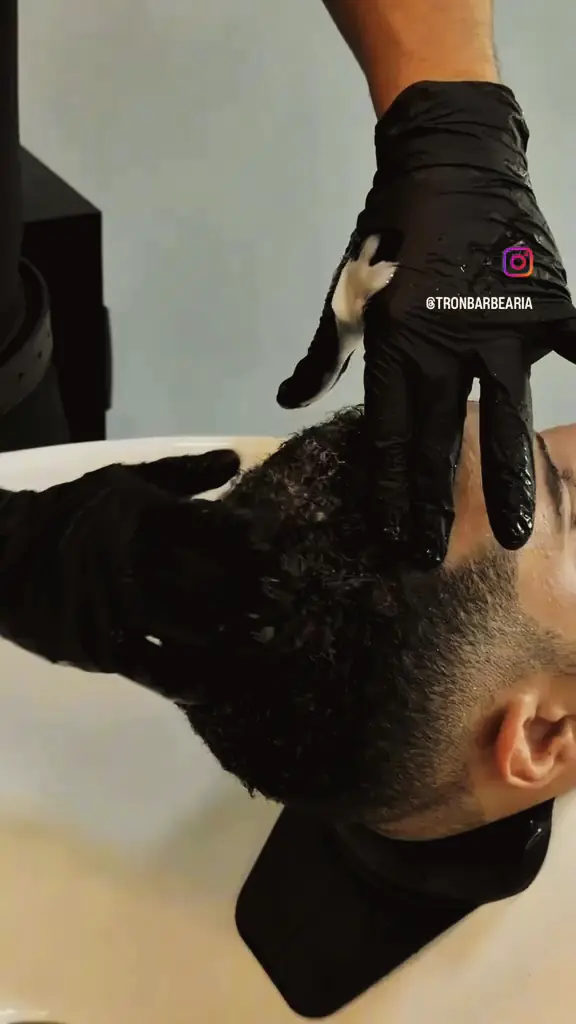Lavagem do cabelo no lavatório com mãos de luvas pretas